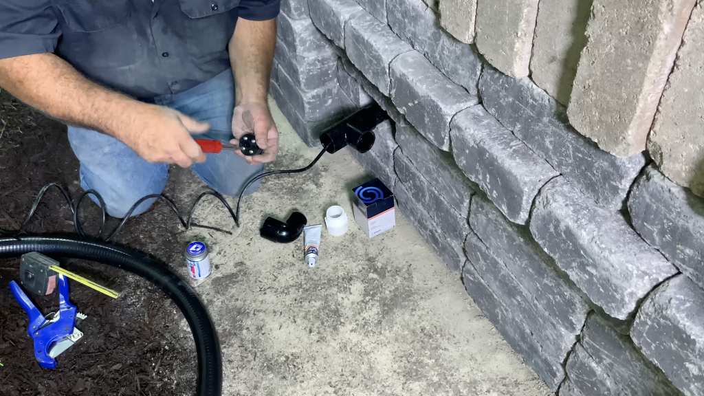 Man installing the cord seal fitting and plumbing to the back side of a hardscape basin for a Stainless Steel Spillway water feature