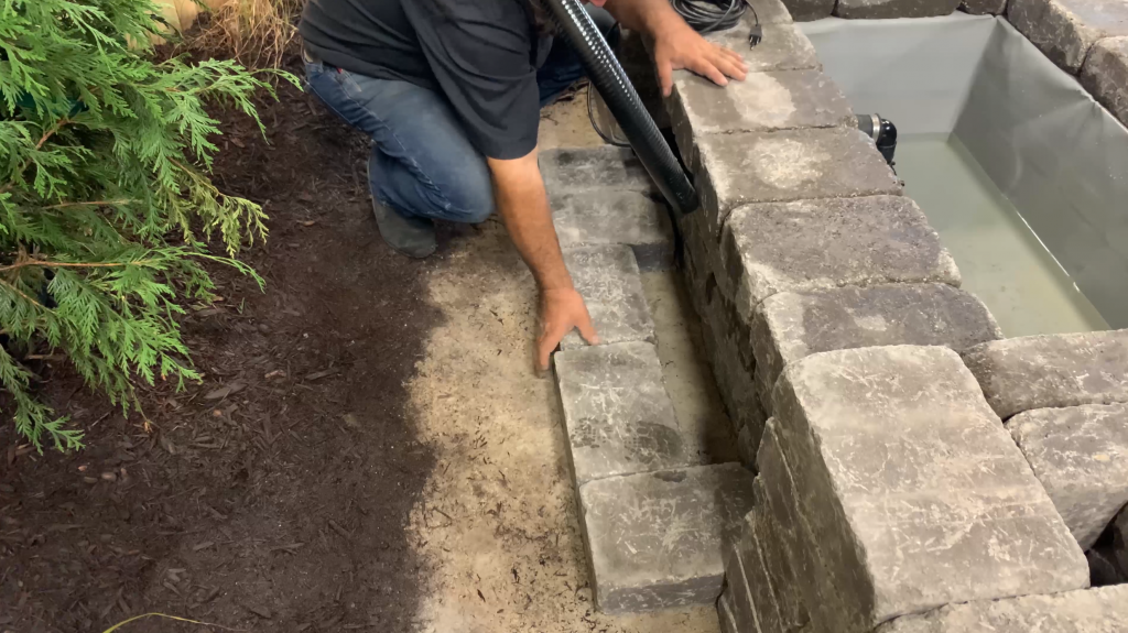 Man creating a double wall to conceal the plumbing of a Copper Spillway Bowl hardscape water feature