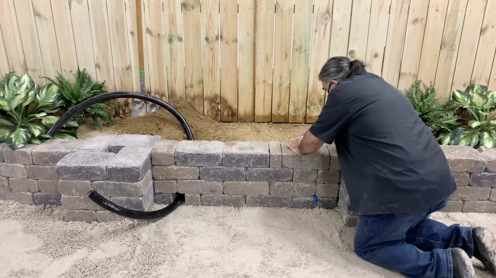 Man installing flexible pvc pipe and funny pipe through a stone wall for a water feature installation