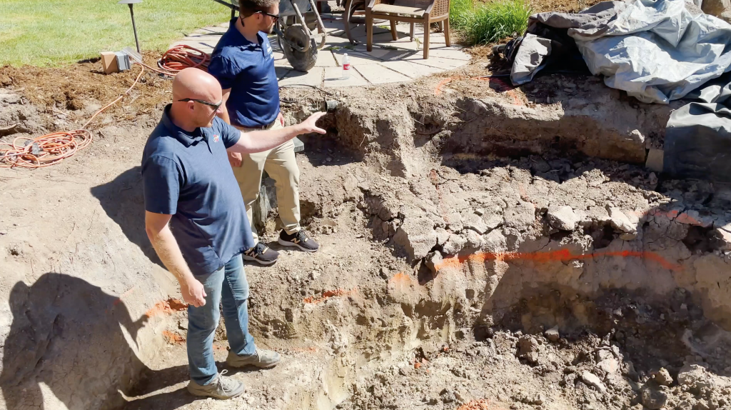 Contractors standing in a dug out pond showing how to create a trench to move ground water from underneath the pond liner